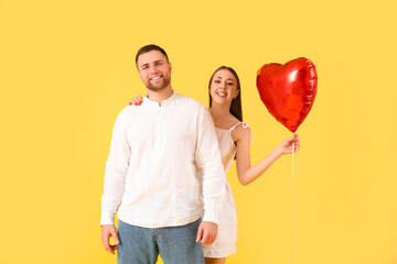 Lovely couple with heart-shaped balloon on yellow background. Valentine's Day celebration