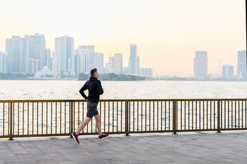 Middle age man wearing sportswear running at seaside. Healthy lifestyle, active city life concept.