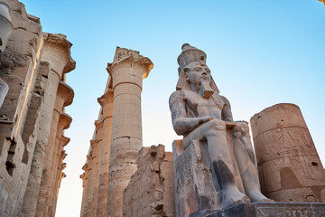 Seated statue of Ramesses II by the First pylon of the Luxor Temple, Egypt. Columns and statues of...