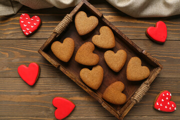 Fototapeta premium Tray with tasty heart shaped cookies and tablecloth on wooden background. Valentine's Day celebration