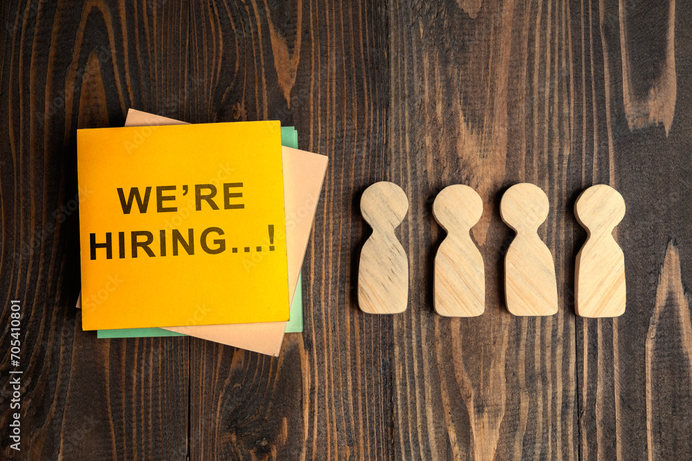 Poster wooden figures and a stack of note paper with we're hiring text