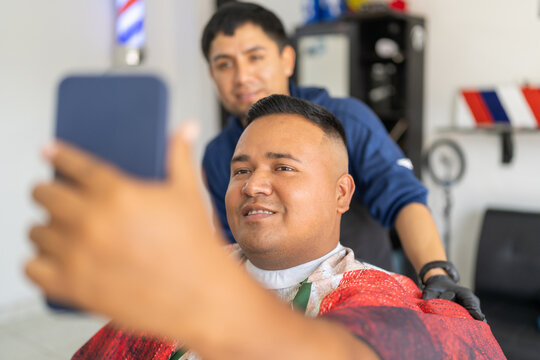 Satisfied client using phone to look himself after cutting hair