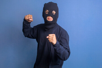 Burglar man in balaclava raising fist showing ready to fight gesture. Concept of crime and violence