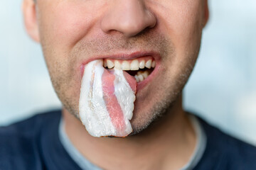 fat bacon in male mouth in close-up. A man eats unhealthy fatty food. - obrazy, fototapety, plakaty