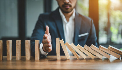 Businessman halts falling domino with hand, symbolic of control and preventing chain reaction
