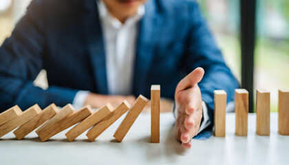 Businessman halts falling domino with hand, symbolic of control and preventing chain reaction - obrazy, fototapety, plakaty