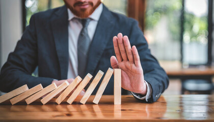 Businessman halts falling domino with hand, symbolic of control and preventing chain reaction