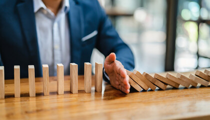 Businessman halts falling domino with hand, symbolic of control and preventing chain reaction