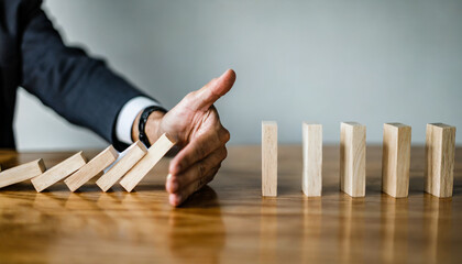 Businessman halts falling domino with hand, symbolic of control and preventing chain reaction