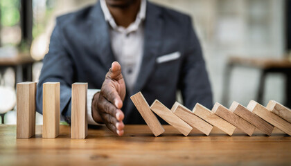 Businessman halts falling domino with hand, symbolic of control and preventing chain reaction - obrazy, fototapety, plakaty