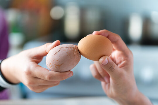 Easter tradition of cracking eggs, two hands hold eggs and try to break each othe egg, close up against blue background