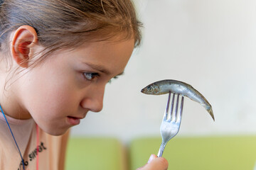 nasty fish. Children don't like to eat fish. teenage girl looks with disdain at a sprat on a fork...
