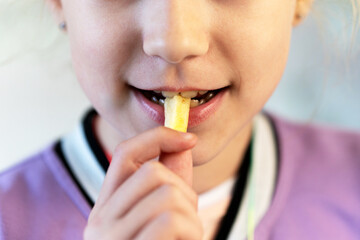 The child eats french fries cheerfully. A little girl opens her mouth to eat a slice of potatoes....