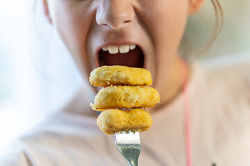 A teenage girl is eating nuggets on a fork. Delicious Chicken nuggets.