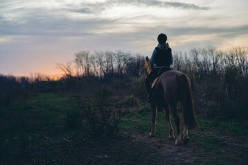 young Latin woman riding her horse in the Argentinean countryside at sunset