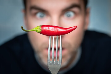 a man is afraid to eat hot peppers. ridiculous expression of a man with hot chillies in his hand