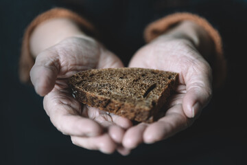 old retired woman holds in her hand a piece of black rye bread on a dark background. The concept of...