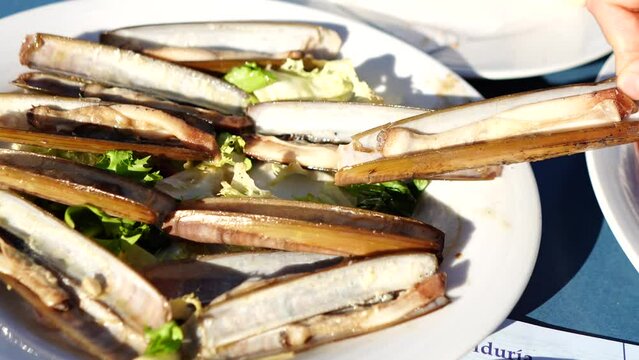 female hand taking grilled sea clam on white plate with lettuce