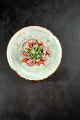 Overhead shot of roast beef carpaccio with Parmesan shavings, arugula, and halved cherry tomatoes on a turquoise plate