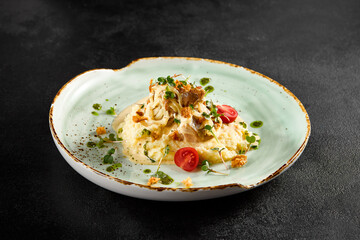 Creamy mashed potatoes topped with tender squid and caramelized onions, garnished with cherry tomatoes on a speckled turquoise plate