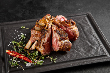 Perfectly grilled lamb rack served on a slate plate, with fresh herbs and a spicy red chili