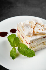 Delicate meringue cake with creamy cheese filling, garnished with a sprig of mint on a white plate