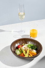 Salad bowl with avocado, vegetables, poached egg, with orange juice and sparkling wine in hard sunlight