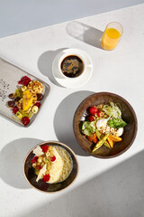 Top view of a hearty breakfast with millet porridge, a salad bowl, syrniki, Americano coffee, and orange juice in sunlight
