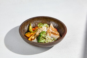 A bowl with grilled chicken, avocado, and mixed vegetables, served in a rustic bowl