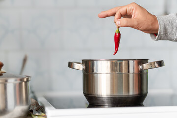 man's hand lays a red hot chili pepper in a saucepan while cooking a meal. small chili pepper