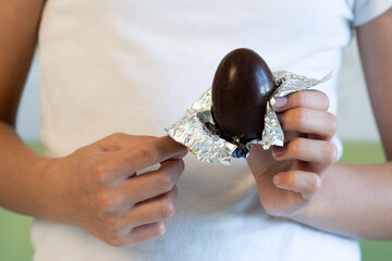 chocolate egg in hands of a teenage girl close-up. A child opens a chocolate egg.