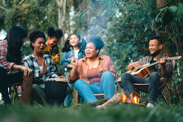 Group of man and woman friends and family singing and playing guitar during having breakfast together. People enjoy and fun outdoor lifestyle travel nature camping on summer holiday vacation.