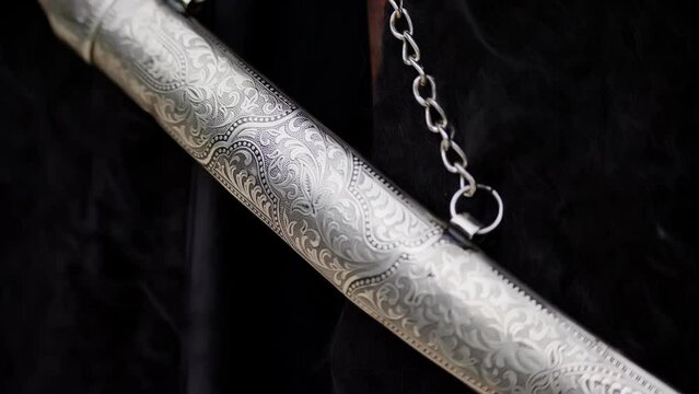 A dagger on a chain hangs on a dark background. Ornament on metal.