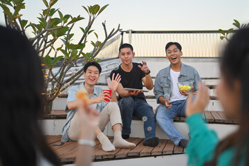 Happy young people gathered together having fun enjoy chill at outdoor rooftop party with drinks.
