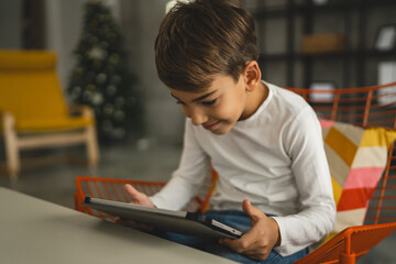 One schoolboy caucasian boy sit at home use digital tablet