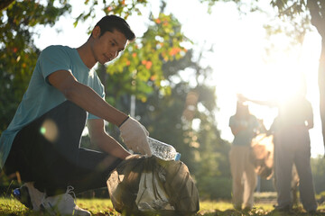 Young man volunteer picking bottles into plastic black bag for cleaning up nature. Environmental...