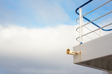 Side-Angle Close-Up of a Ship Horn on a Grey Deck with Blue and White Railing, Under a Cloudy...