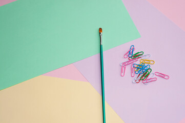 Paint brush and paper clips on a colorful background. Flat lay. Creative minimal concept. No people.