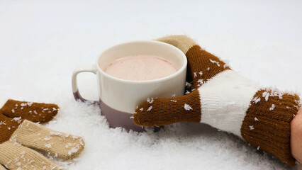 Tasty hot chocolate in a mug in the snow, held by hand with glove.