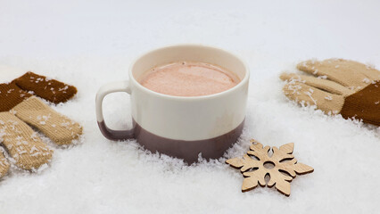 Tasty hot chocolate in a mug stands in the snow with gloves and a wooden snow crystal.
