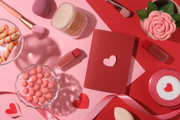 Valentine’s Day card mockup with lipstick, cushion, sweet candy and ribbon decorated on pink and red background. Blank space on red card for design. Top view