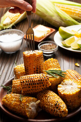 Female taking  grilled sweet corn piece from plate with the fork