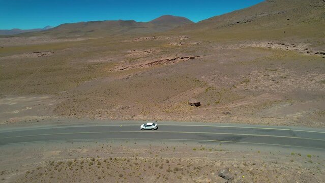 Beautiful aerial footage of a car driving alone in the dessert road of the Atacama - Calama - Antofagasta Dessert and Salar - turquoise lagoon 