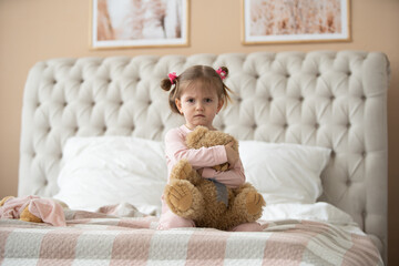 Cute little girl in pajama hugging her toy hare on the bed at home, happy childhood concept