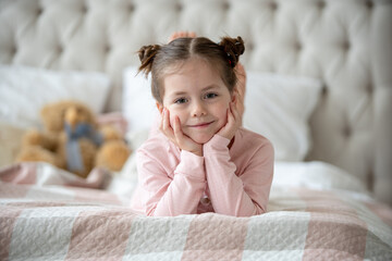 Cute little girl in pajama hugging her toy hare on the bed at home, happy childhood concept