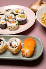 Chop sticks, mushrooms, noodle ramen, California rolls and Philadelphia rolls on a small plate on a pink background

