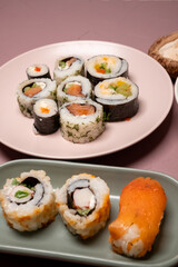 Chop sticks, mushrooms, noodle ramen, California rolls and Philadelphia rolls on a small plate on a pink background
