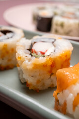 Chop sticks, mushrooms, noodle ramen, California rolls and Philadelphia rolls on a small plate on a pink background
