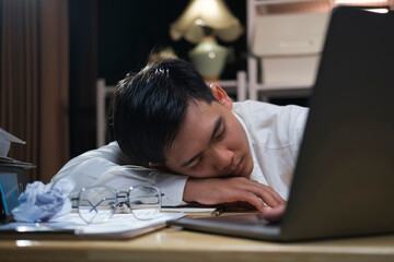 Young tired businessman lying on table at night office..