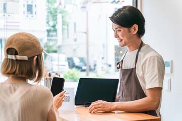 カフェのレジ・会計で電子決済・スマホ決済に対応するカフェ店員
